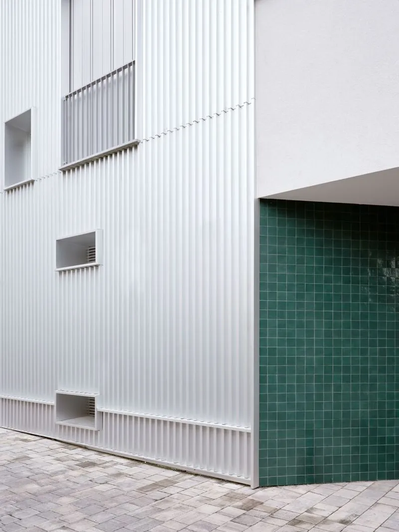Ground level courtyard entrance with vertical white cladding and dark green tile wall