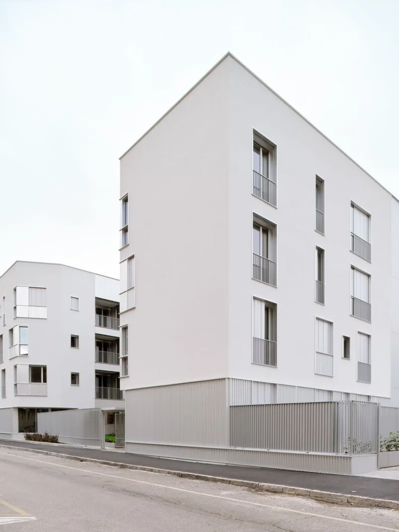 Street view of the white rendered facade with recessed balconies and corrugated metal ground floor cladding