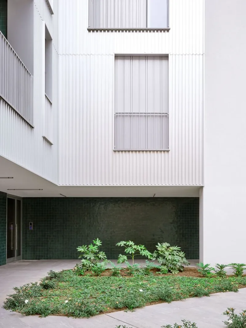 Interior courtyard with planted bed beneath white corrugated facade and green tile wall