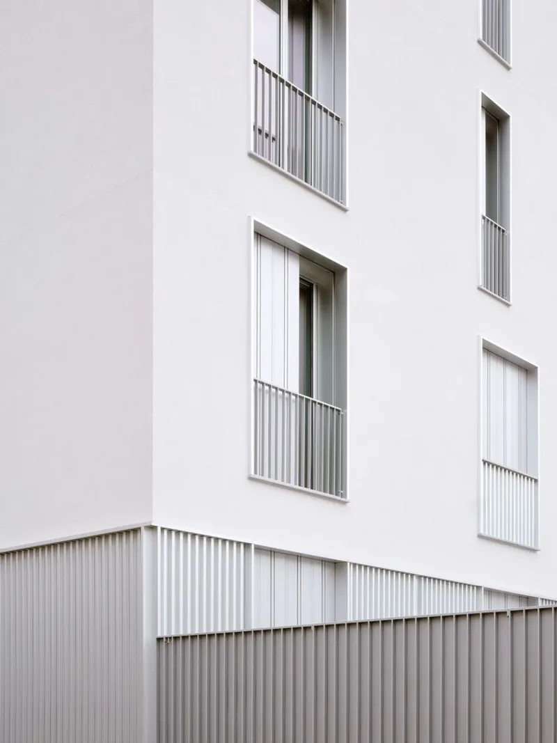 Facade detail showing stacked balconies with metal railings above corrugated base cladding