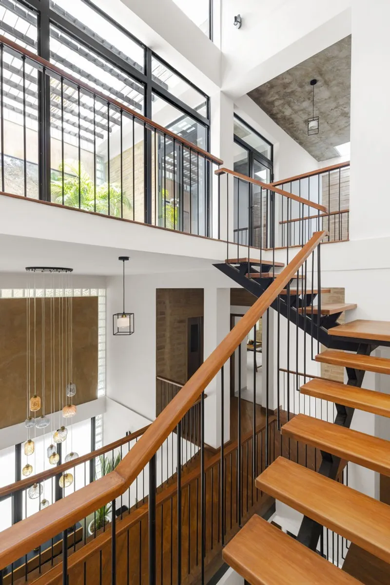 Double-height stairwell with timber treads and black steel stringers below a slatted skylight