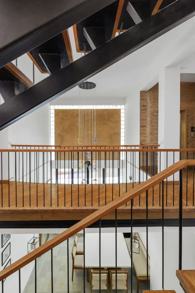 View through the upper landing railing toward a backlit brick wall with pendant chandelier