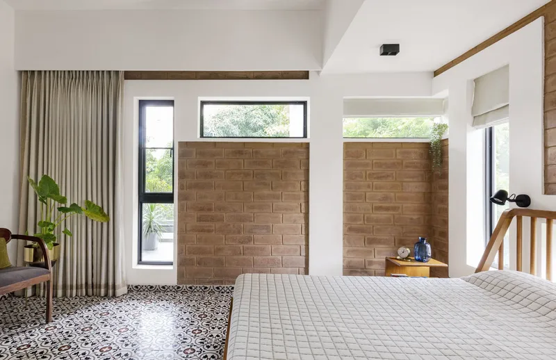 Bedroom with patterned terrazzo floor meeting a brick partition wall beneath clerestory windows