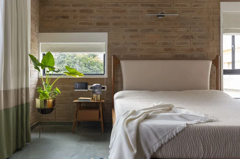 Bedroom with exposed brick wall, upholstered headboard, and potted plant near a horizontal window