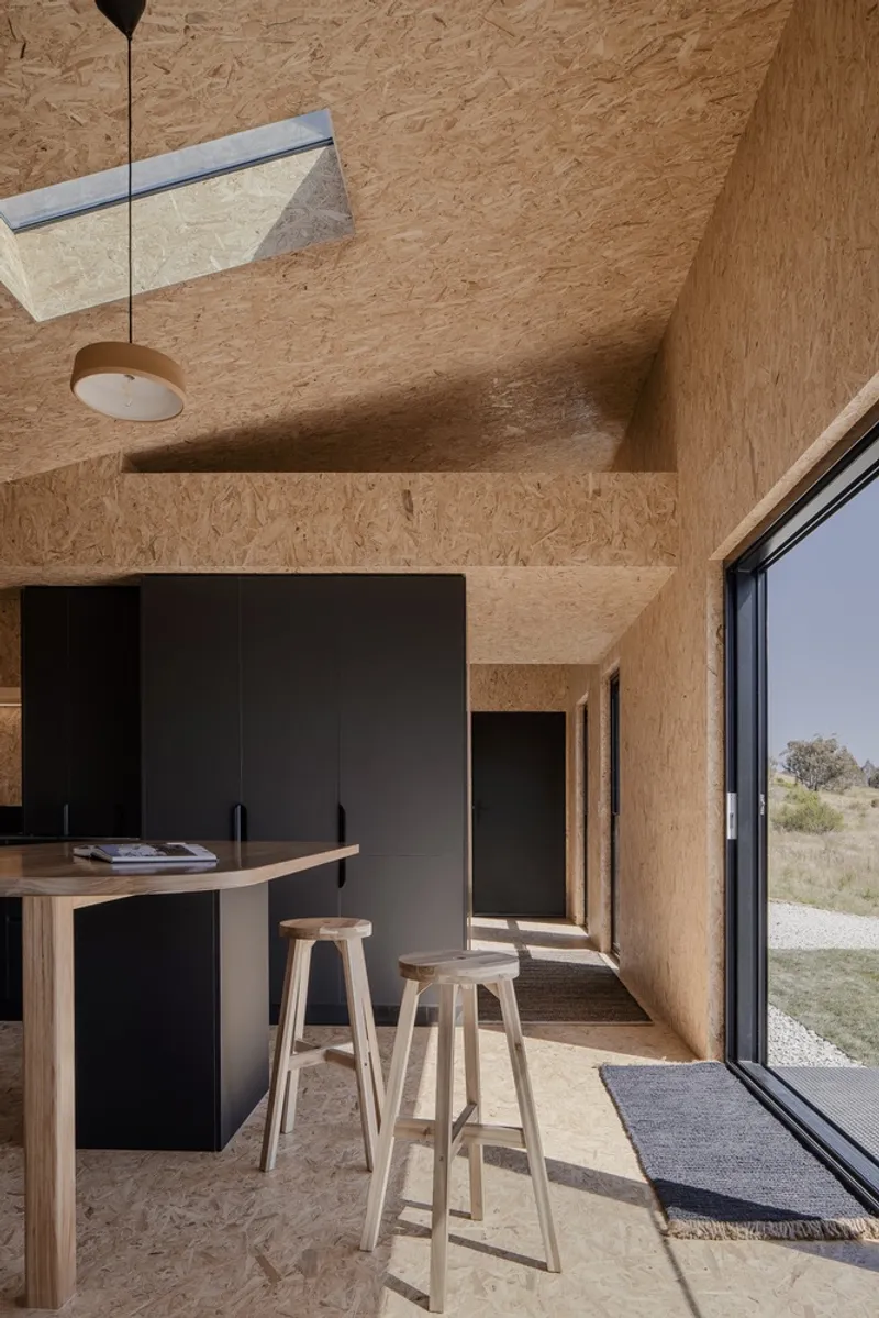 Kitchen with oriented strand board walls and ceiling featuring a skylight and timber bar stools
