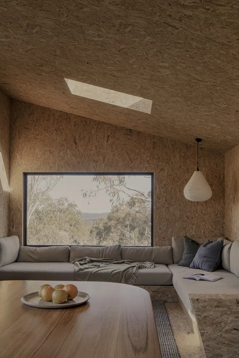 Living room with oriented strand board surfaces and a horizontal window framing the surrounding bushland