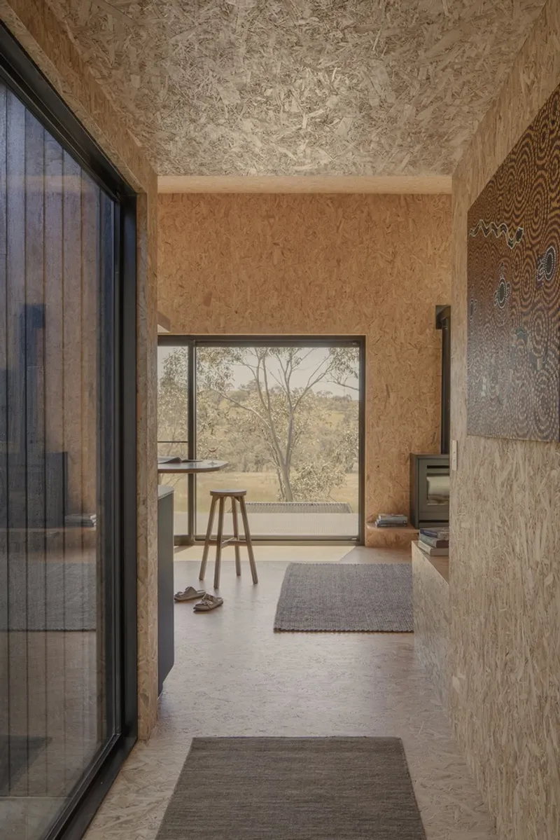 Hallway view through oriented strand board walls toward a picture window overlooking distant eucalyptus trees