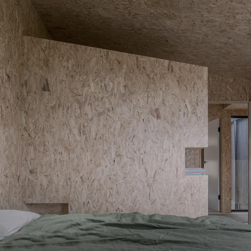 Bedroom with oriented strand board walls and ceiling featuring a recessed storage niche above the bed