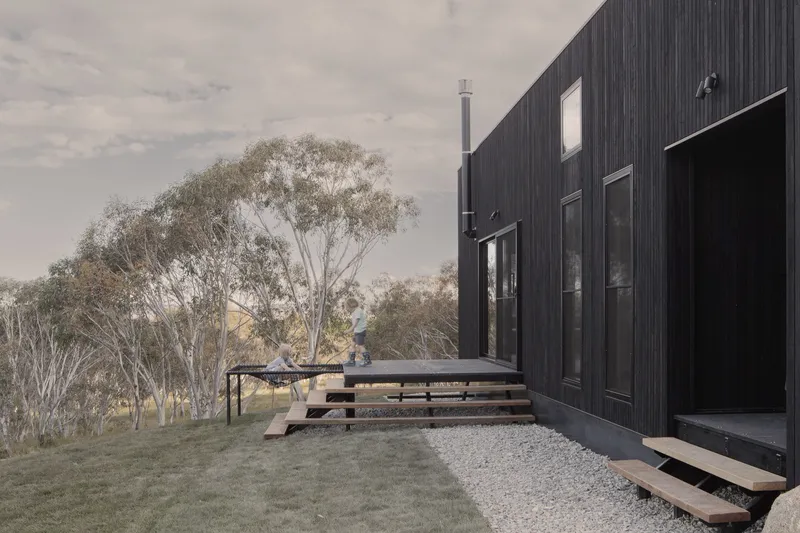 Black vertical timber facade with stepped timber benches and gravel courtyard beside native trees