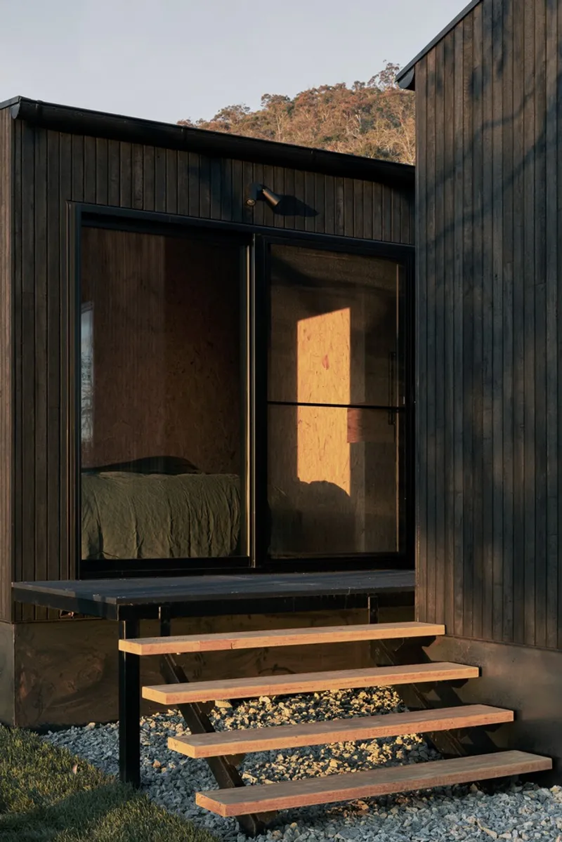 Exterior timber steps leading to glazed bedroom opening at dusk with warm interior light