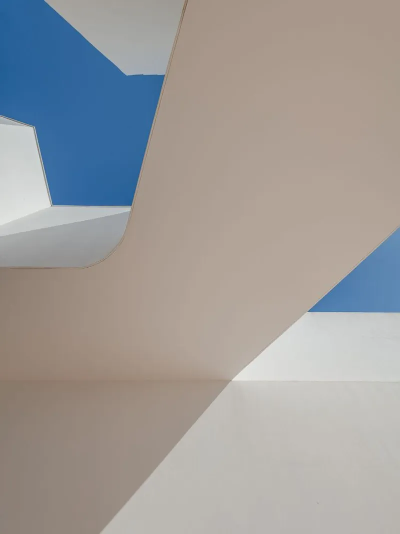 Abstract view of courtyard ceiling planes and angular skylight openings revealing clear blue sky