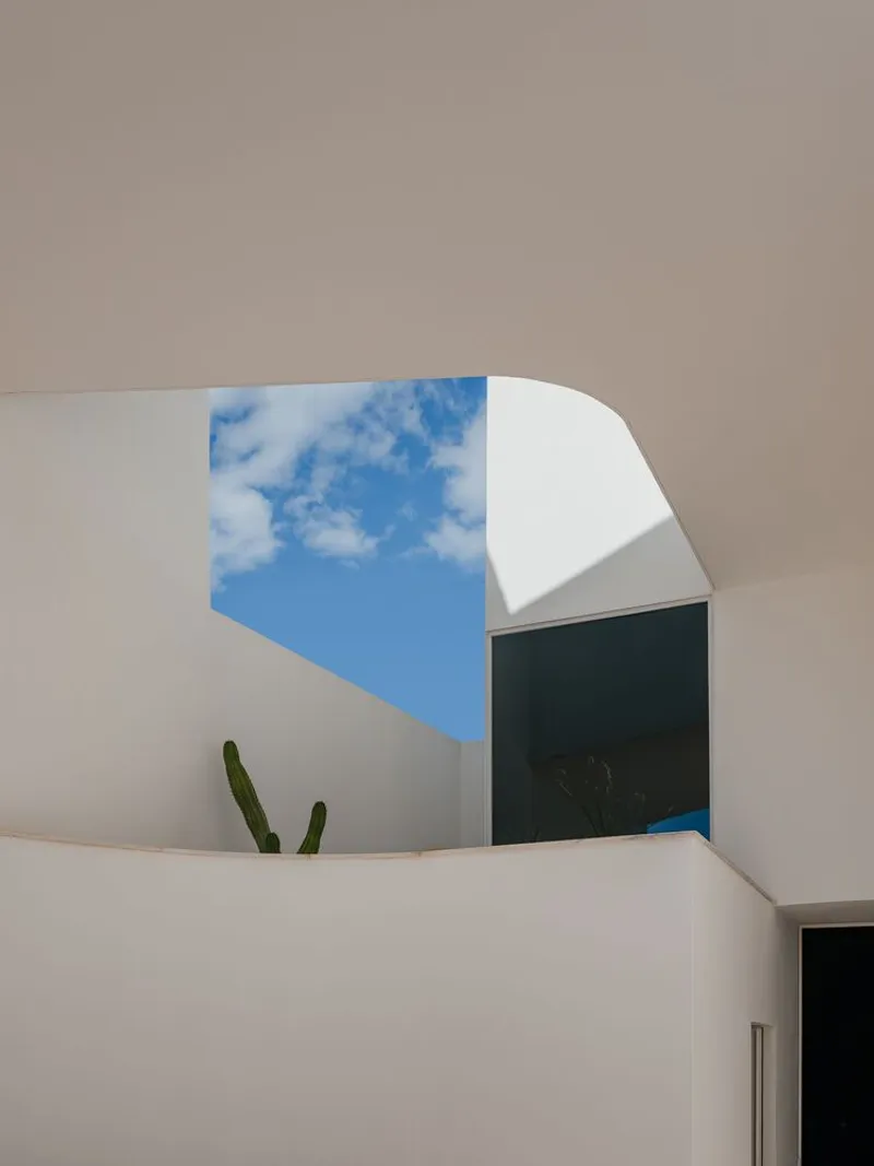 Upward view through angular courtyard opening framing blue sky and cactus planted in corner alcove