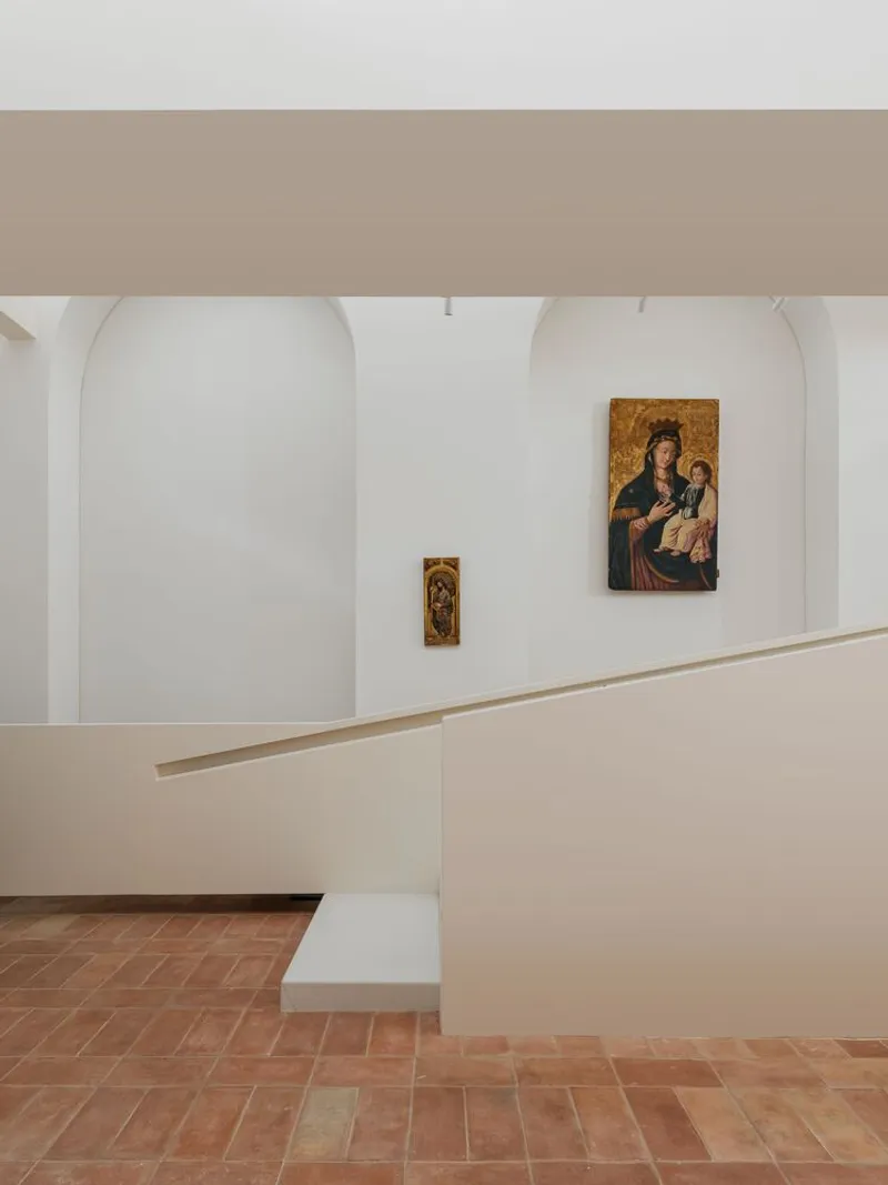 Curved white balustrade overlooking gallery space with religious paintings mounted in arched alcoves