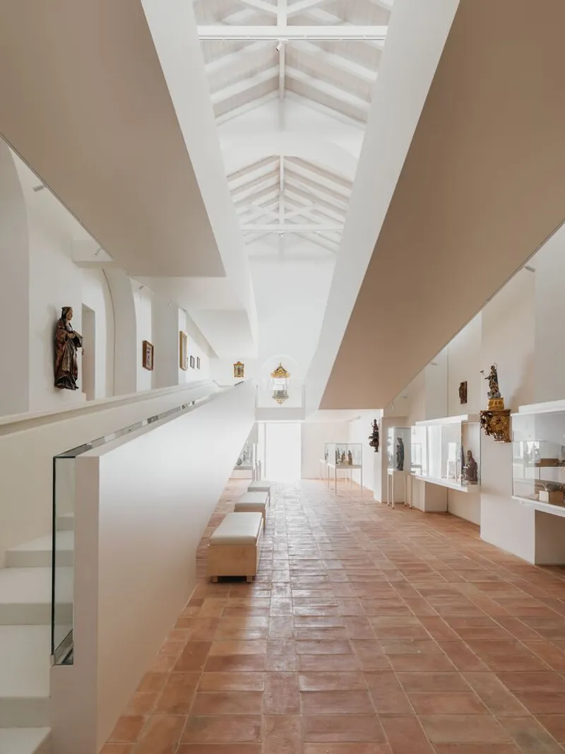 Upper gallery corridor with exposed white timber roof trusses and terracotta tile floor stretching into distance
