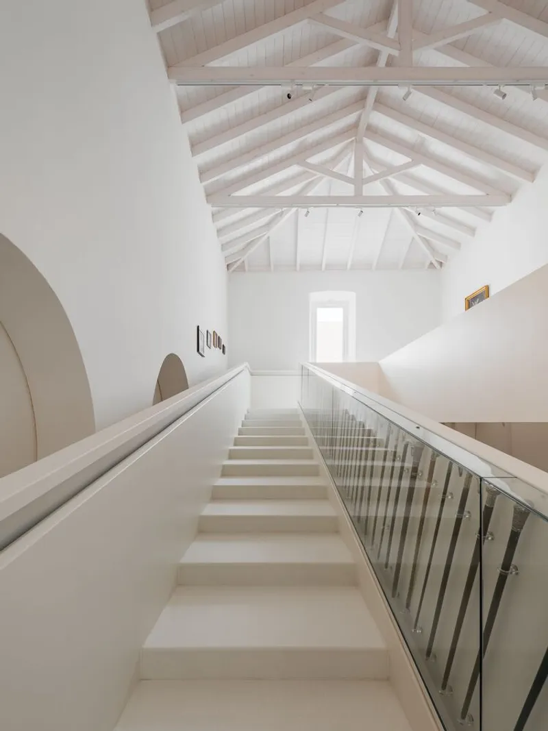 Staircase rising toward exposed timber roof structure with central skylight above white plastered walls