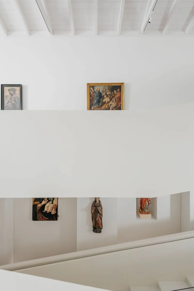 View across gallery levels showing white parapet walls with displayed artworks and sculptures in niches below