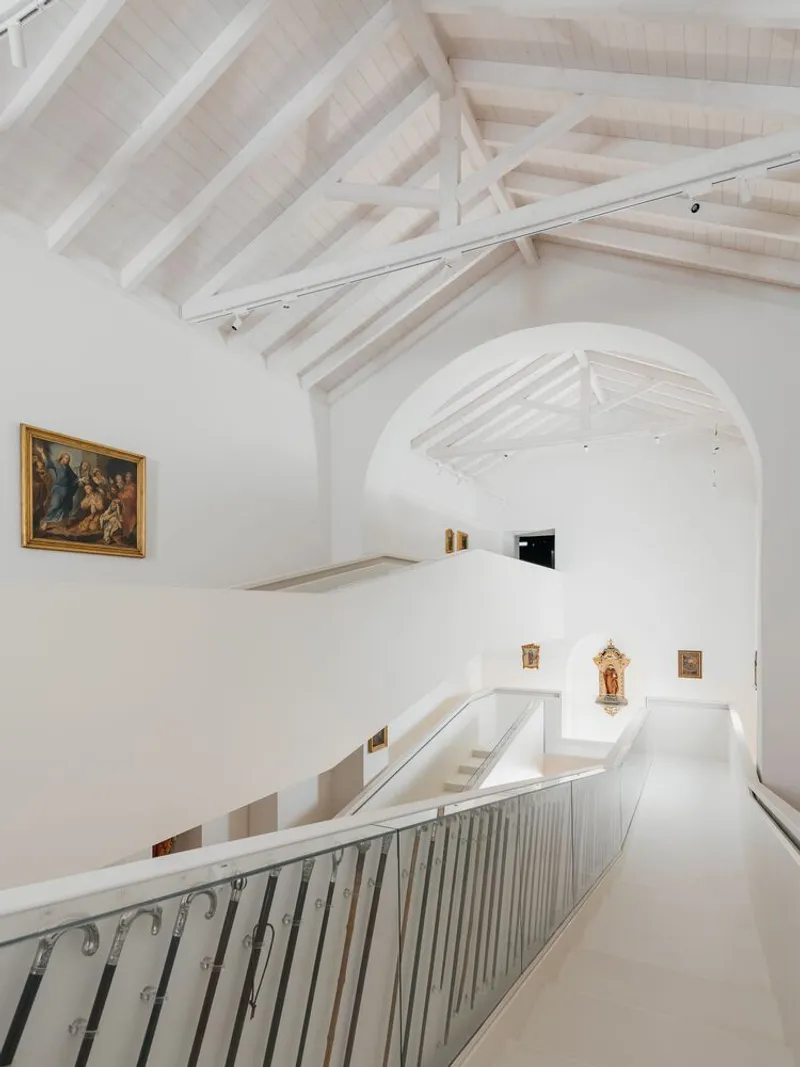 Upper gallery corridor with vertical metal balustrade and arched opening framing timber truss ceiling structure