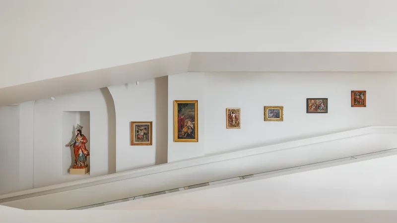 Upper gallery level with sculpture in arched niche and framed paintings along white parapet wall