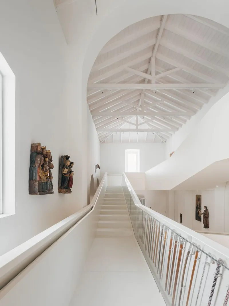Bridge walkway with metal railing spanning between upper gallery levels beneath exposed timber truss ceiling