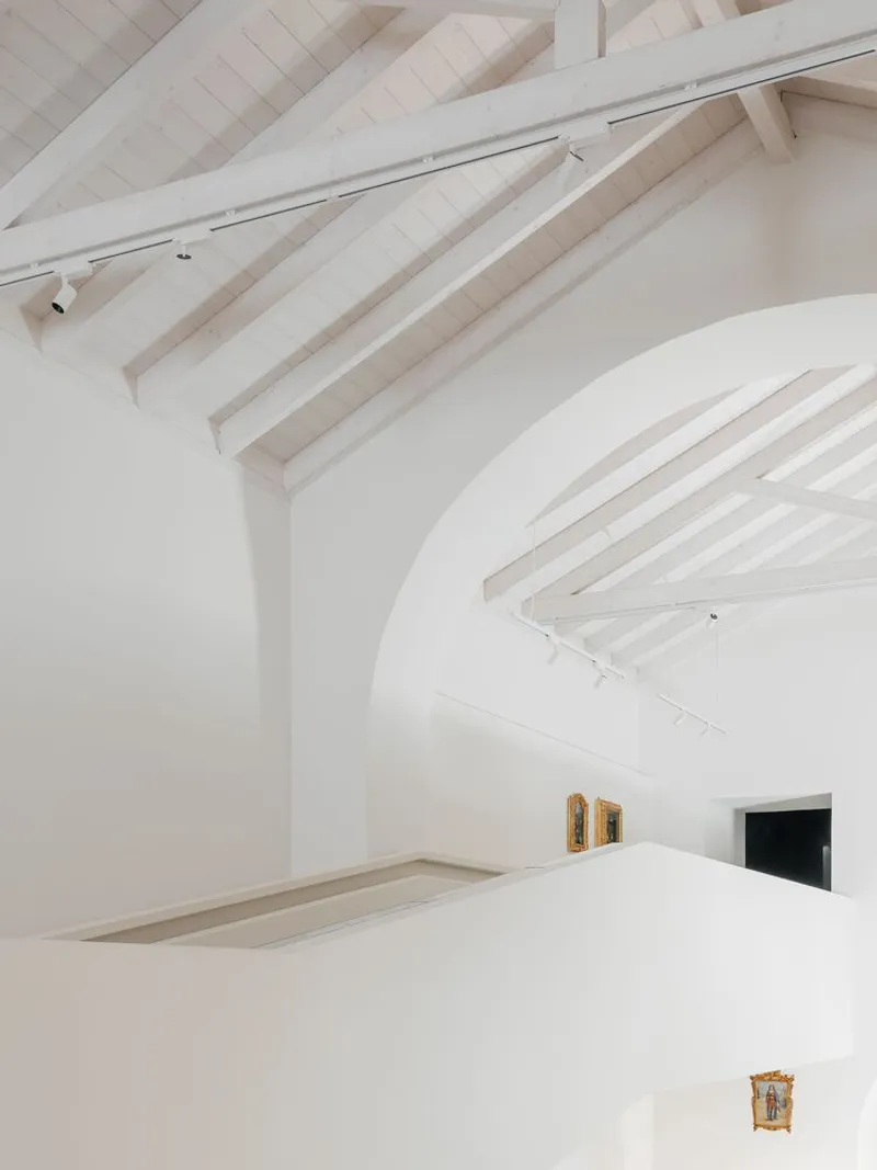 Detail of intersecting white barrel vaults with exposed timber roof rafters and track lighting mounted above