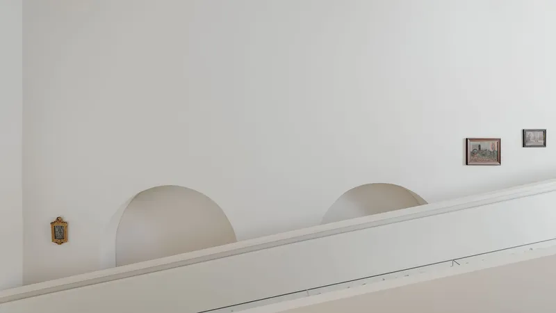White plastered wall with arched alcoves and framed artworks hung at intervals