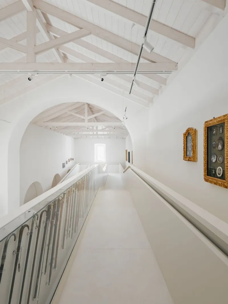 Upper gallery walkway with metal balustrade and artworks on the white wall