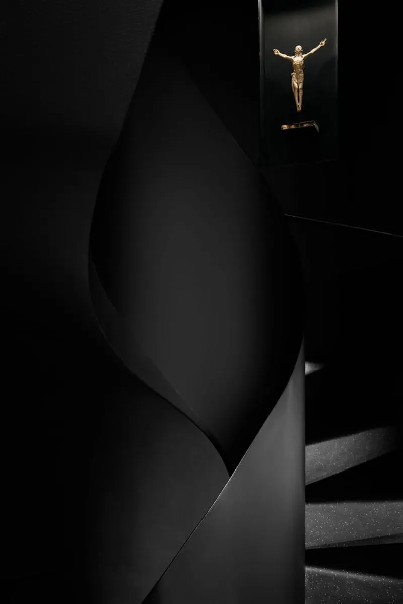 Interior stairwell with black angled walls and a crucifix illuminated in a recessed niche above