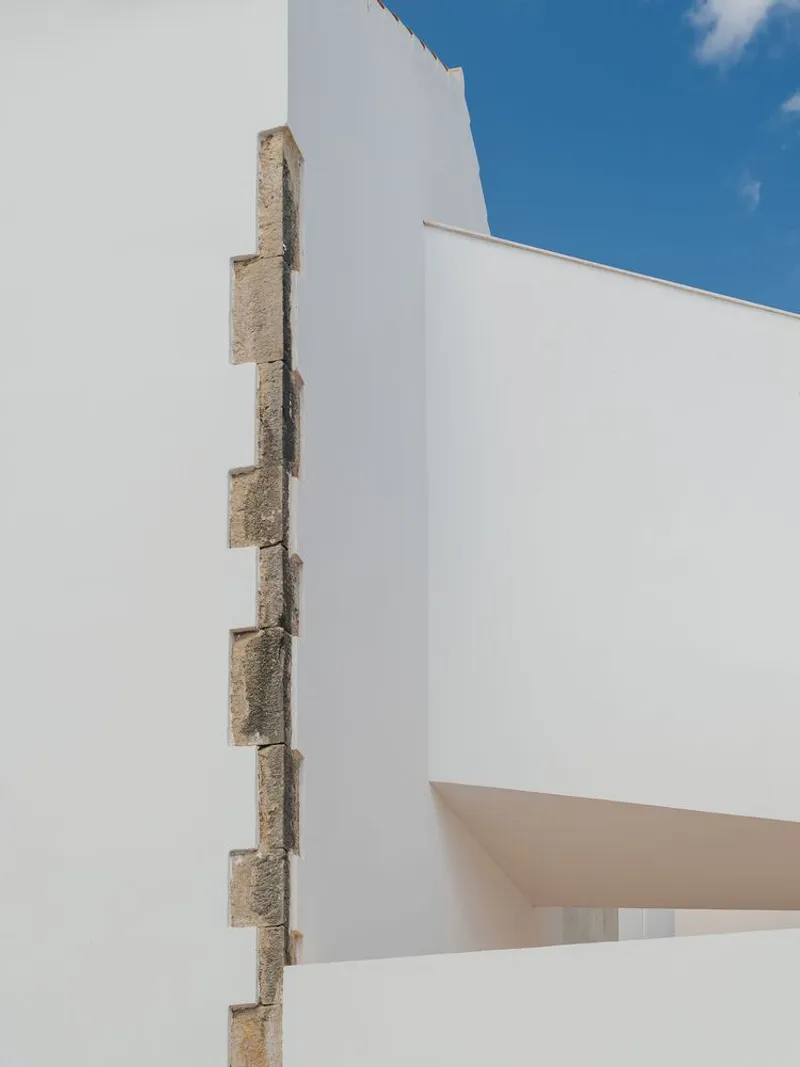 Vertical stone reveal detail against white stucco volumes under a blue sky with clouds