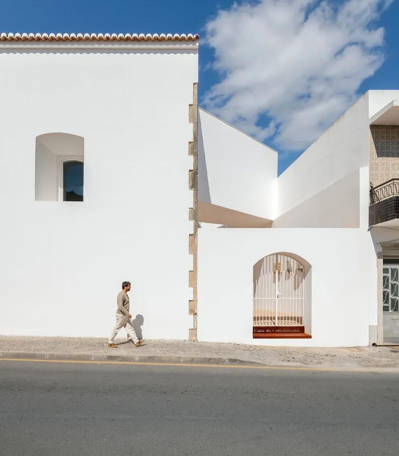 Street facade with arched openings and cantilevered volume as a pedestrian walks past in daylight