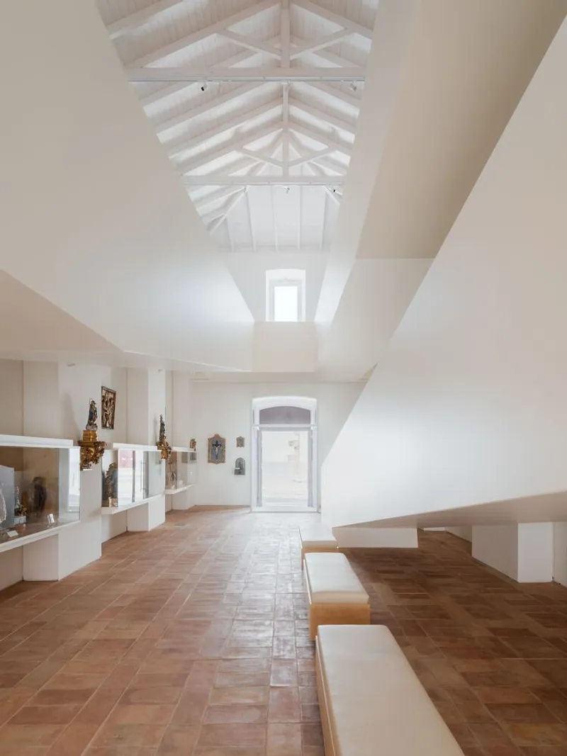 Gallery interior with exposed timber roof trusses and terracotta floor tiles under natural light
