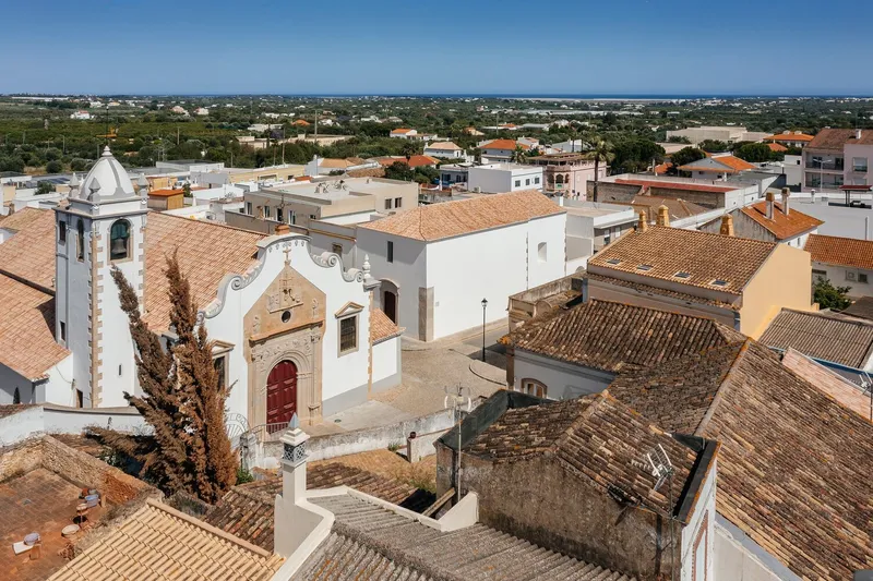 Elevated view of a white church with bell tower and terracotta rooftops in a low-rise town