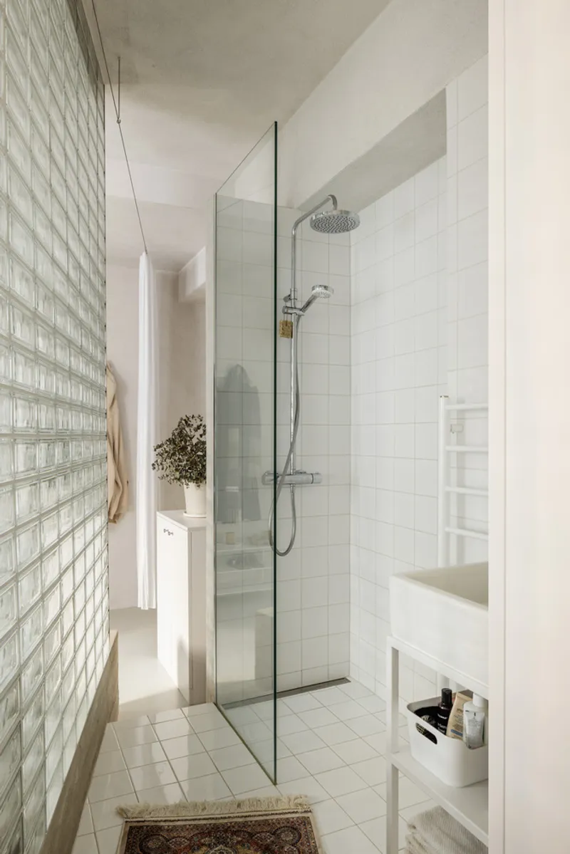 Bathroom with glass shower enclosure and white tile walls next to a translucent glass block partition