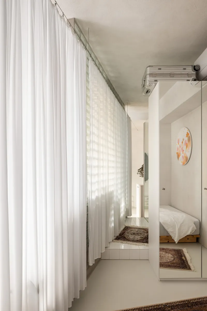 Floor-to-ceiling sheer curtain beside a glass block wall with a white column framing the bedroom beyond