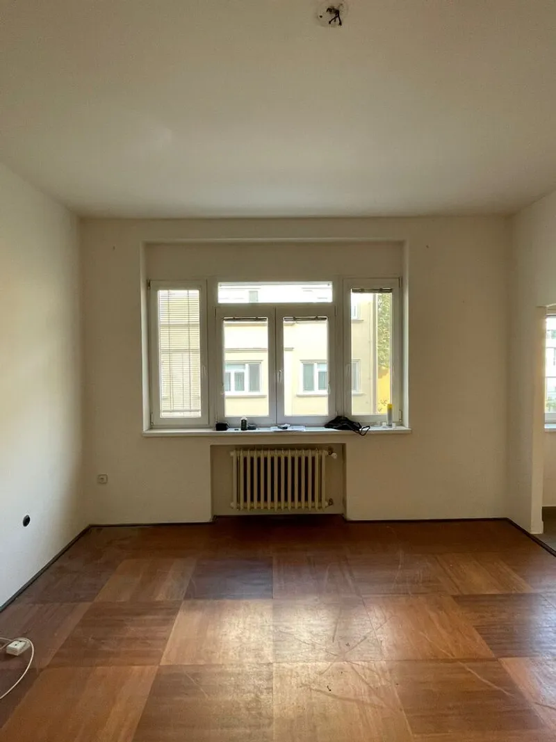 Window alcove with exposed radiator below and parquet wood flooring in daylight