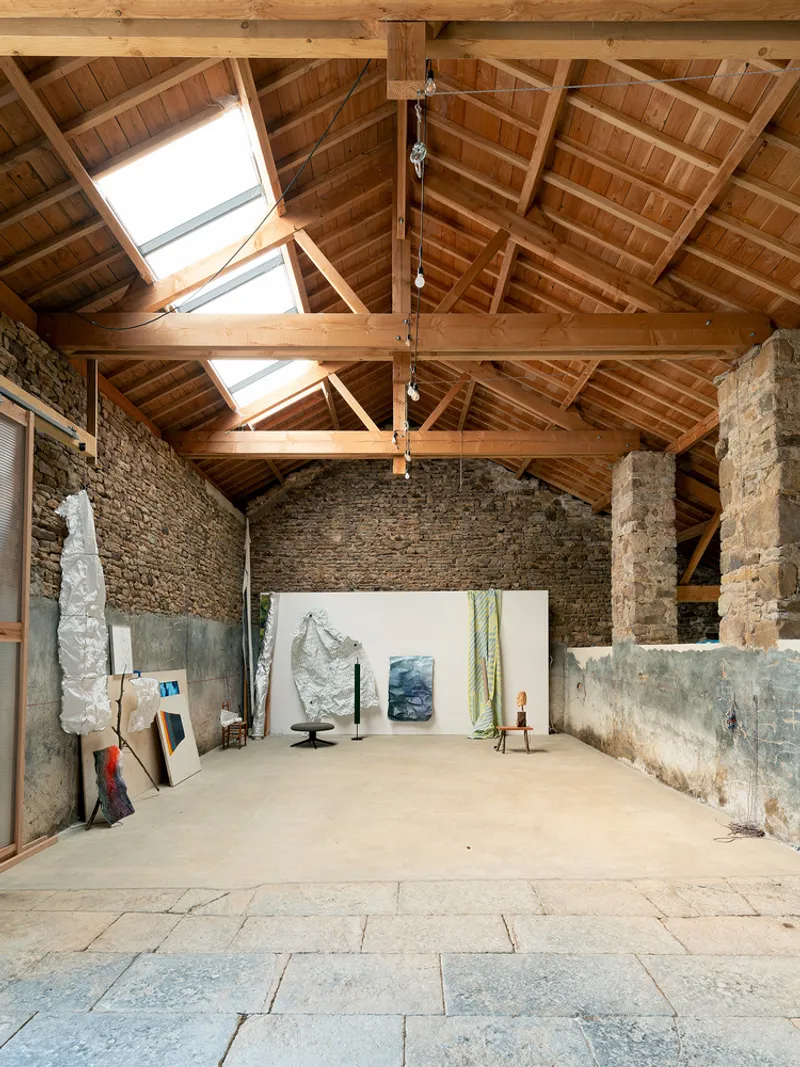 Interior studio space with exposed timber roof trusses and skylights above stone walls