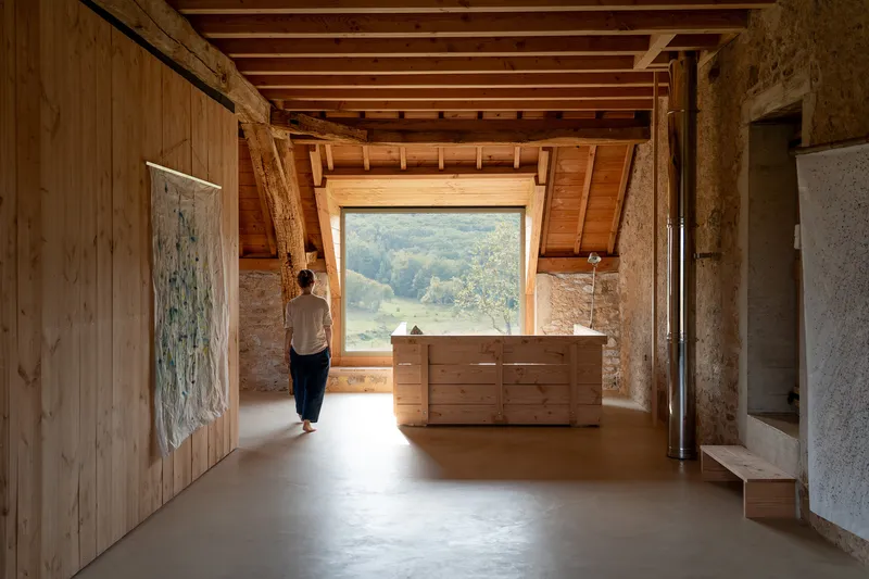 Person standing in timber-lined room with pitched ceiling beams and large landscape window