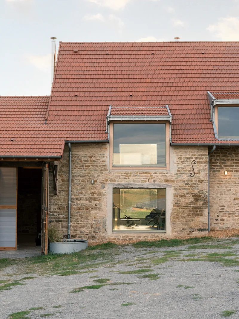 Two large windows cut into the weathered stone wall beneath a clay tile roof