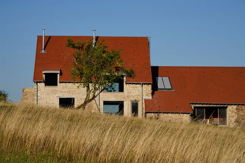 Stone and brick facade with orange clay tile roof emerging above golden dry grass