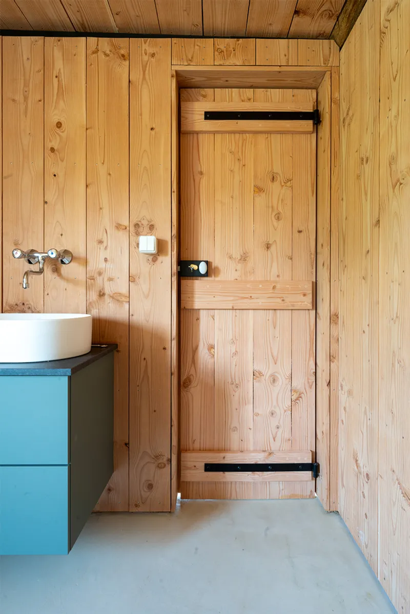 Pine-clad bathroom with black iron hinges on the door and a blue sink cabinet