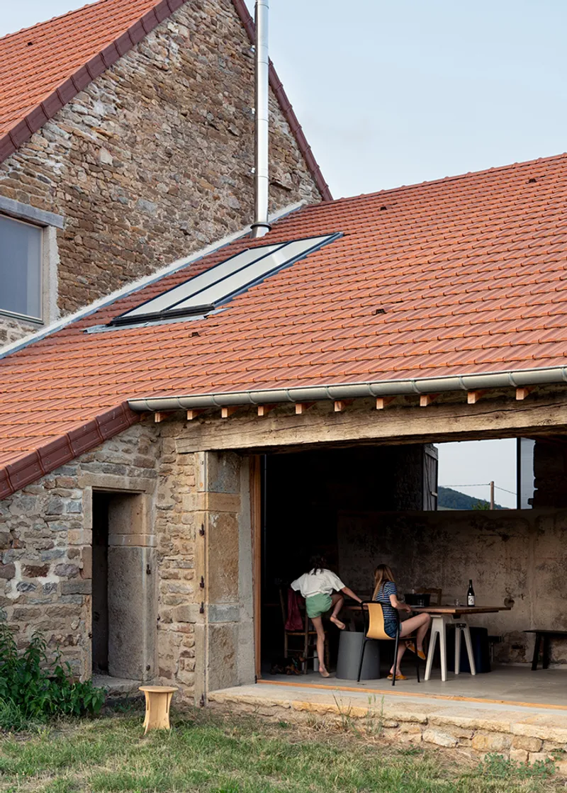 Open-air covered terrace beneath the clay tile roof with two people preparing a meal at dusk