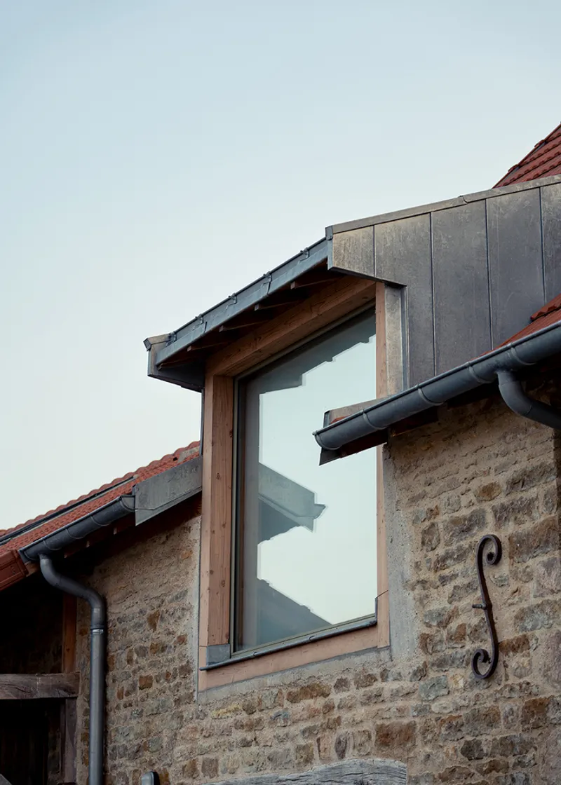 Detail of dormer window with timber frame and zinc cladding emerging from the clay tile roof