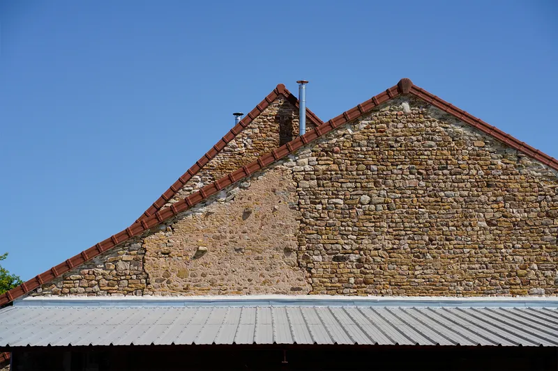 Gable end with layered stone masonry and red clay tile roof under a clear blue sky