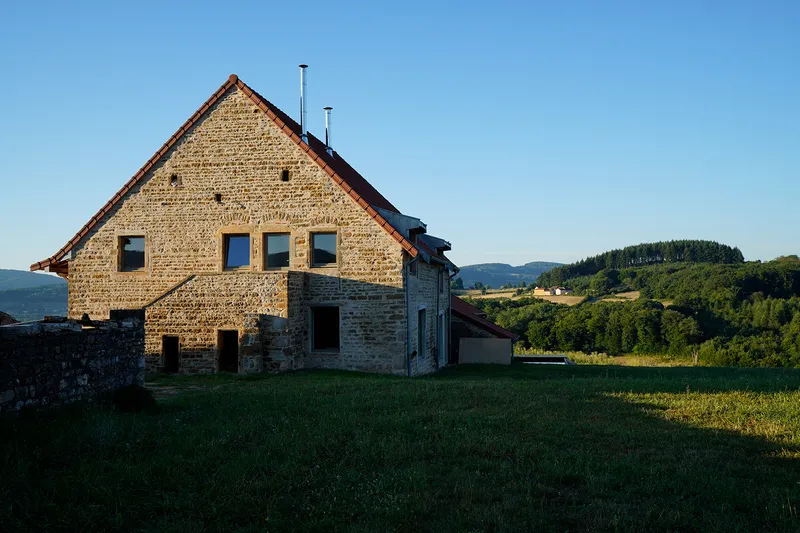 Stone barn with gabled roof and square windows set on a grassy slope at dusk