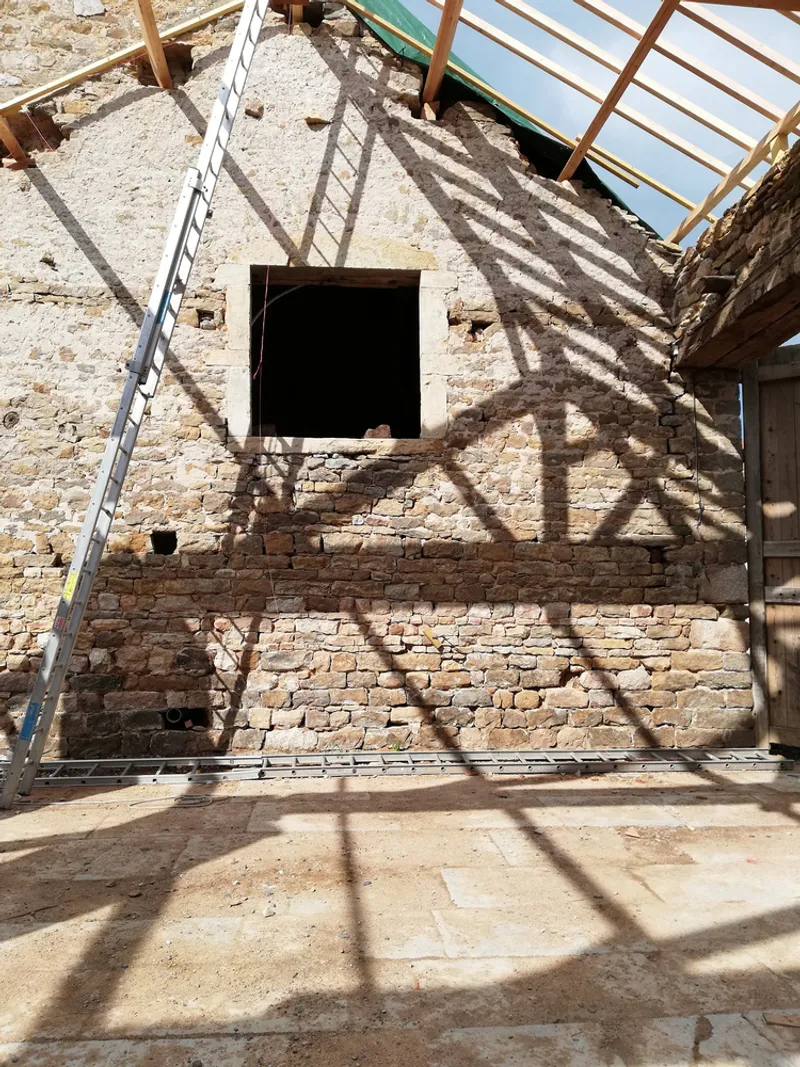 Interior stone wall with square opening casting rafter shadows from skylight above