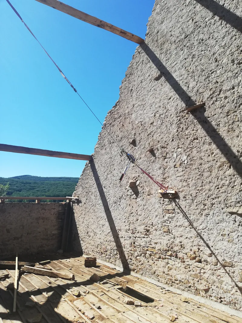 Rough stone gable wall with steel beams and construction cable under clear blue sky