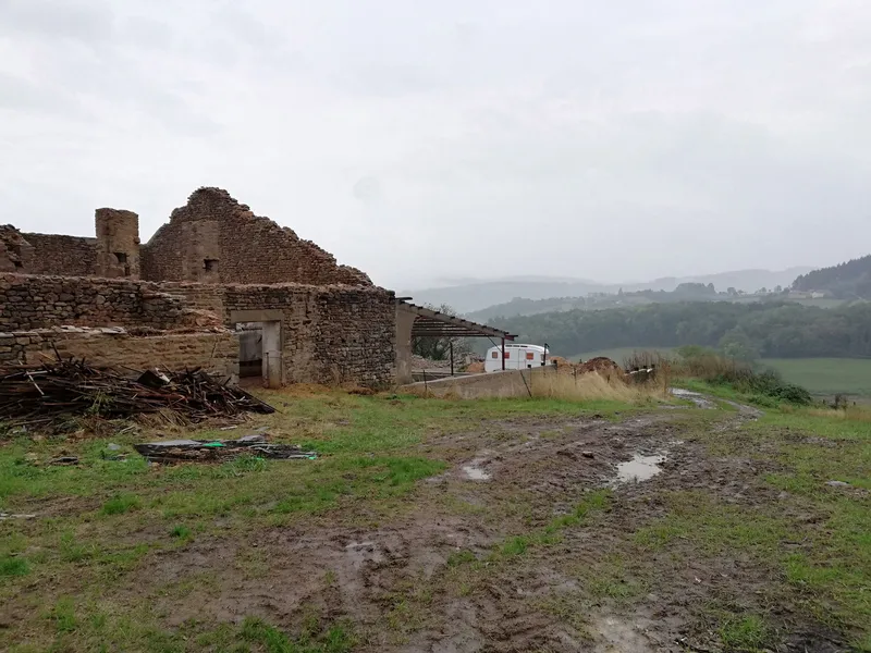 Roofless stone ruin with timber columns on muddy ground under overcast skies