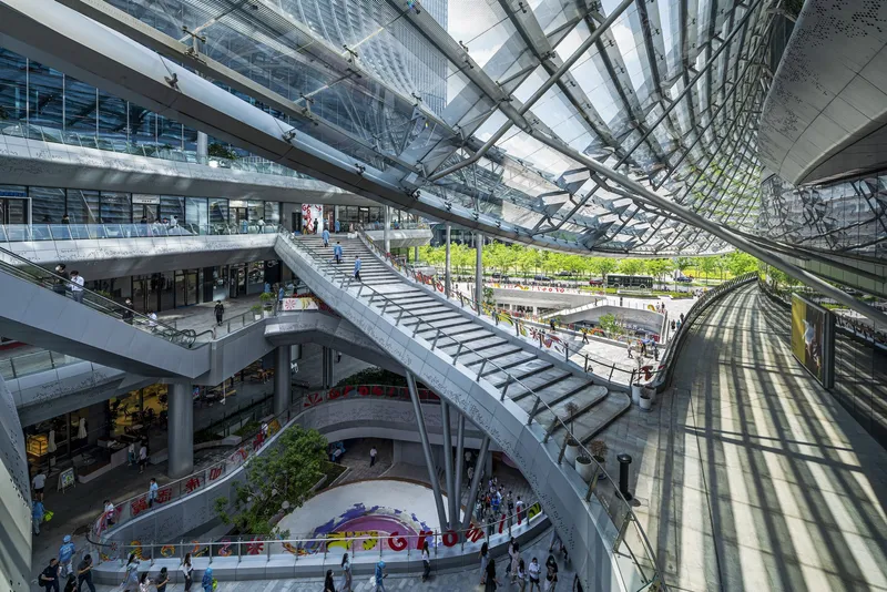 Multi-story atrium with diagonal steel staircase rising through planted terraces and glass skylight overhead