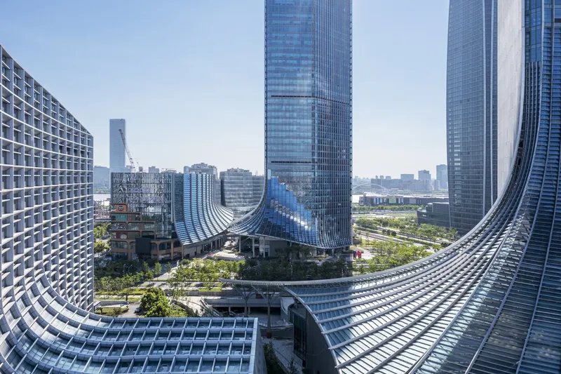 View through curved glass facade showing undulating tower podium and surrounding highrise skyline