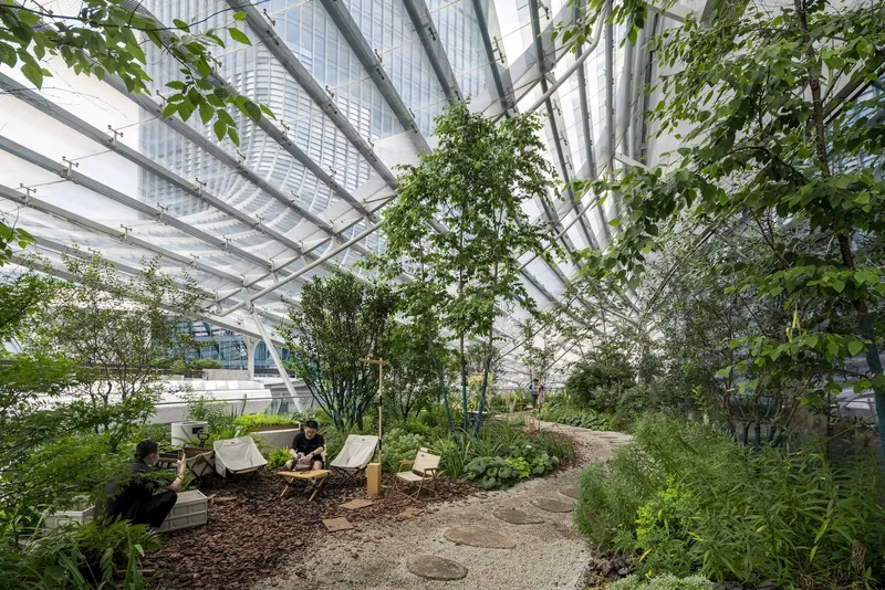 Planted rooftop terrace with gravel path, lounge chairs and trees beneath diagonal steel and glass canopy