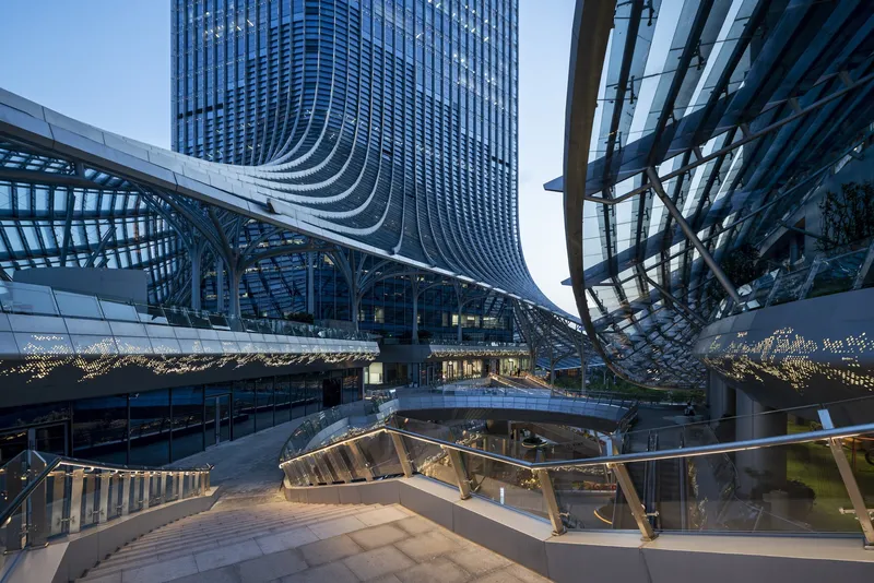Evening view of central plaza with curved bridges and tower facade rising behind glass canopy